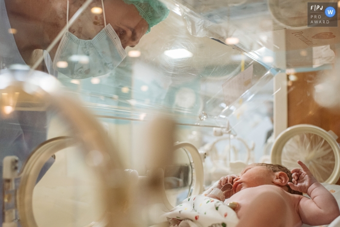 Photo by: <a href="https://www.fpja.com/documentary-family-photography-contests/claudia-ruiz/rio-de-janeiro/2111684">Claudia Ruiz - Brazil</a> Maternidade Perinatal Laranjeiras hospital birthing image showing father watching baby inside incubator