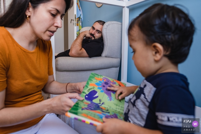 Photo by: <a href="https://www.fpja.com/documentary-family-photography-contests/raquel-oczerny/sao-paulo/2111049">Raquel O'Czerny - Brazil</a> Sao Paulo at home Day in the Life photography showing dad watching his son reading with mommy
