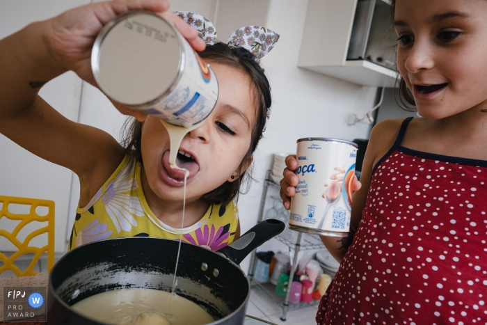 Photo by: <a href="https://www.fpja.com/documentary-family-photography-contests/raquel-oczerny/sao-paulo/2111074">Raquel O'Czerny - Brazil</a> Sao Paulo Day in the Life documentary family photo showing a younger sister licking the sugar while preparing a recipe