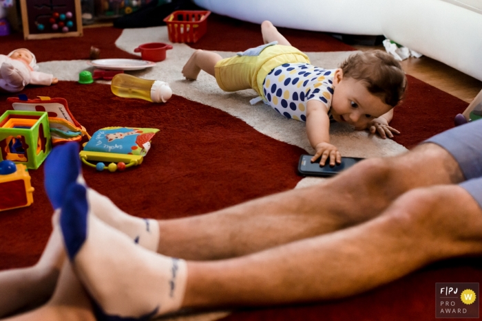 Photo by: <a href="https://www.fpja.com/documentary-family-photography-contests/marine-poron/paris/2111272">Marine Poron - France</a> Ile-de-France at home Day in the Life photography showing the baby wants to grab the cellphone