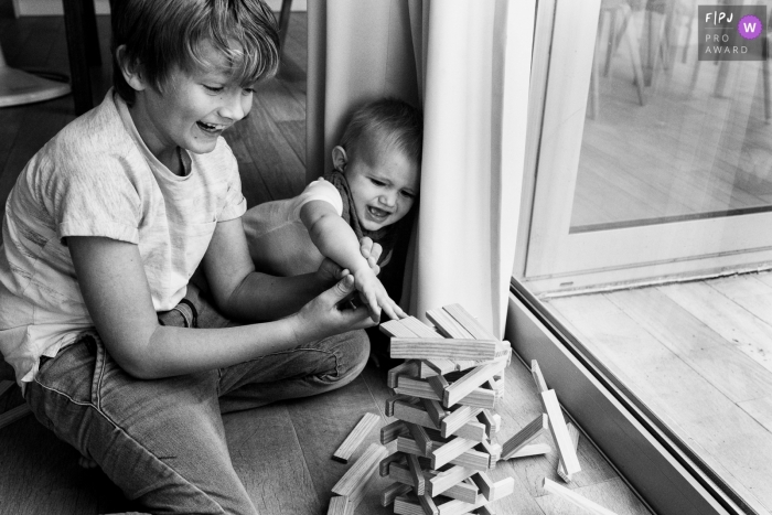 Day in the Life photography session at home in Flanders with kids playing by the window with wooden stacking block game Day in the Life photography session at home in Flanders with kids playing by the window with wooden stacking block game