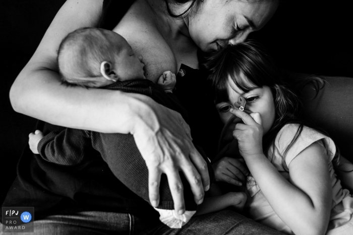 Photo by: <a href="https://www.fpja.com/documentary-family-photography-contests/thiago-braga/florianopolis/2111693">Thiago Braga - Brazil</a> Florianopolis, Santa Catarina at home Day in the Life photography of a mother breastfeeding her newborn baby, on the sofa at home, with her eldest daughter receiving affection together