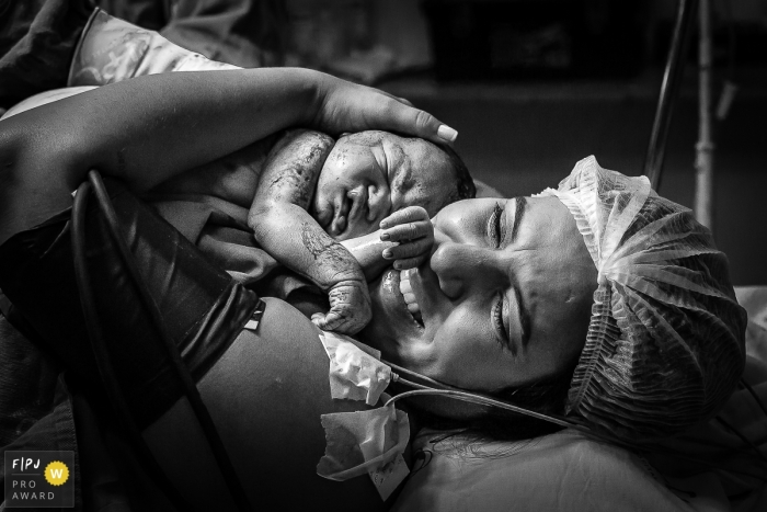 Image de photojournalisme de naissance de l'hôpital Plantadores de Cana de l'émotion pure d'une mère tenant son nouveau bébé.