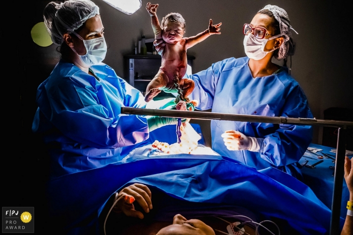 Moment driven São Luiz Anália Franco birth photojournalism image of a newborn being held up right after being born by cesarrean