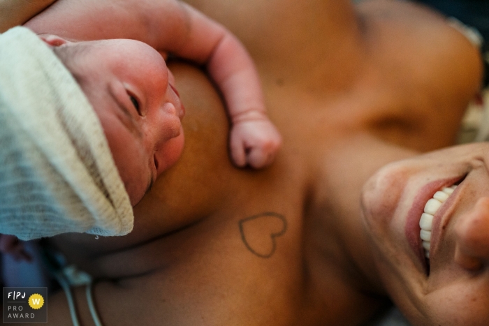 Moment driven Neocenter Maternidade birth photojournalism image. This is a moment of great joy for the mother for having the daughter who was just born in her arms. She smiled proudly, without stopping for her husband.