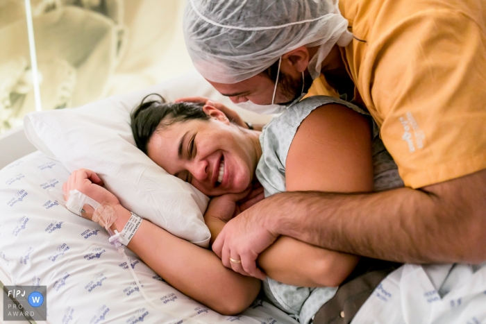 Moment driven Hospital e Maternidade São Luiz birth photojournalism image of a couple embracing with smiles on the day of their baby's birth Moment driven Hospital e Maternidade São Luiz birth photojournalism image of a couple embracing with smiles on the day of their baby's birth