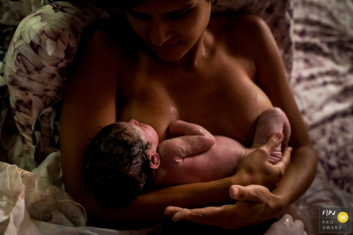 Image de photojournalisme de naissance à domicile axée sur le moment montrant le premier contact avec la peau pour le nouveau bébé