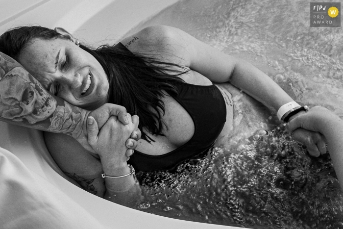  Moment driven Maternidade Perinatal Barra birth photojournalism image showing a bathtub to relax in the hot water, the mother cries in pain and despair for not knowing how much time is left to finish the labor. the husband and the doula hold her hand