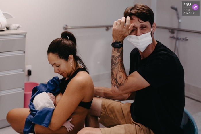 Moment driven Maternidade Ilha birth photojournalism image showing an emotional dad as mom feeds baby Moment driven Maternidade Ilha birth photojournalism image showing an emotional dad as mom feeds baby