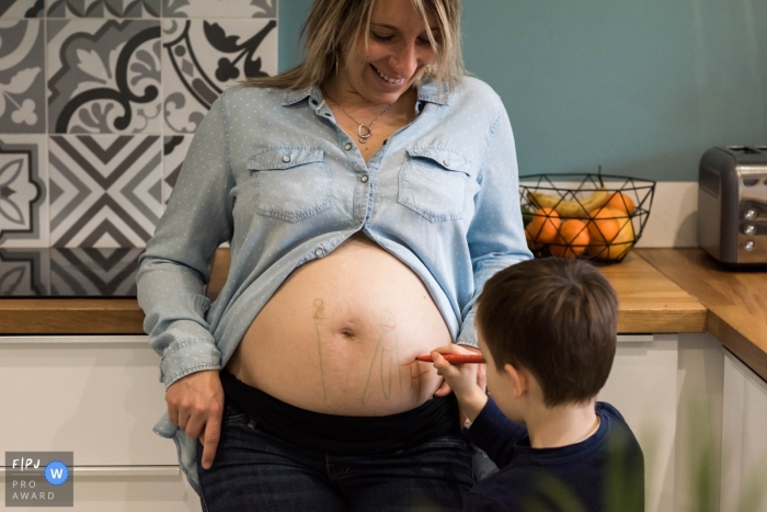 Photographie de famille landaise animée par l'instant d'un jeune garçon faisant un dessin sur le ventre de femme enceinte de sa mère