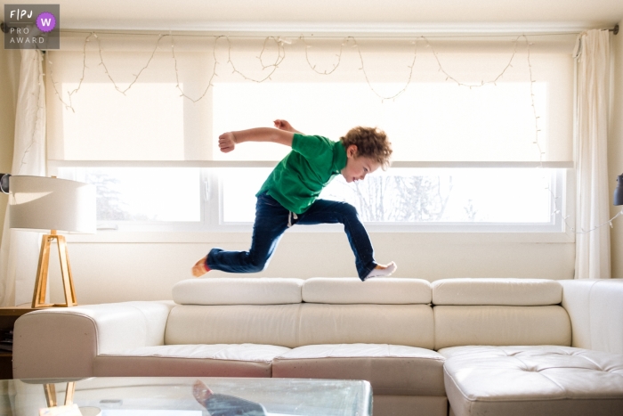 Photo by: <a href="https://www.fpja.com/documentary-family-photography-contests/viara-mileva/kingston/2112075">Viara Mileva - Canada</a> Moment driven Ontariio, Canada family photojournalism image of a boy jumping on the couch, breaking some rules