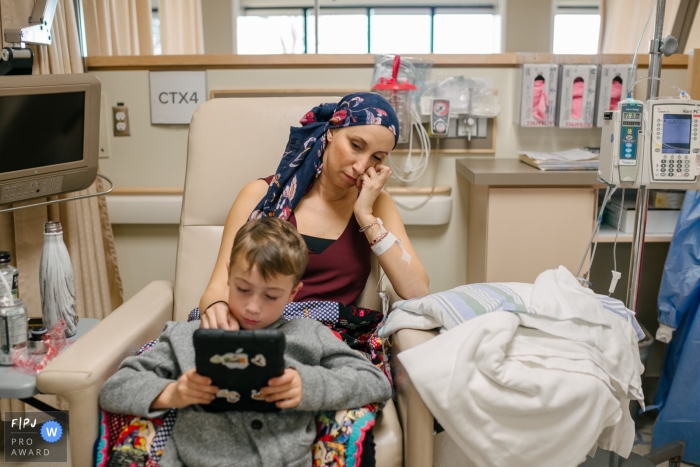 Photo by: <a href="https://www.fpja.com/documentary-family-photography-contests/viara-mileva/kingston/2112080">Viara Mileva - Canada</a> Moment driven Kingston family photojournalism image of a boy sitting with his mother during a chemotherapy treatment