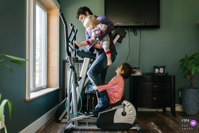 Une photographie de famille de Kingston captivée par un moment capturant un père jongle avec deux enfants qui essaient constamment de grimper sur l'équipement d'exercice