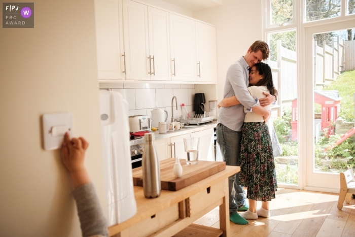 Moment driven Gloucestershire family photojournalism image of tired parents hugging while their child tries to turn the light on Moment driven Gloucestershire family photojournalism image of tired parents hugging while their child tries to turn the light on