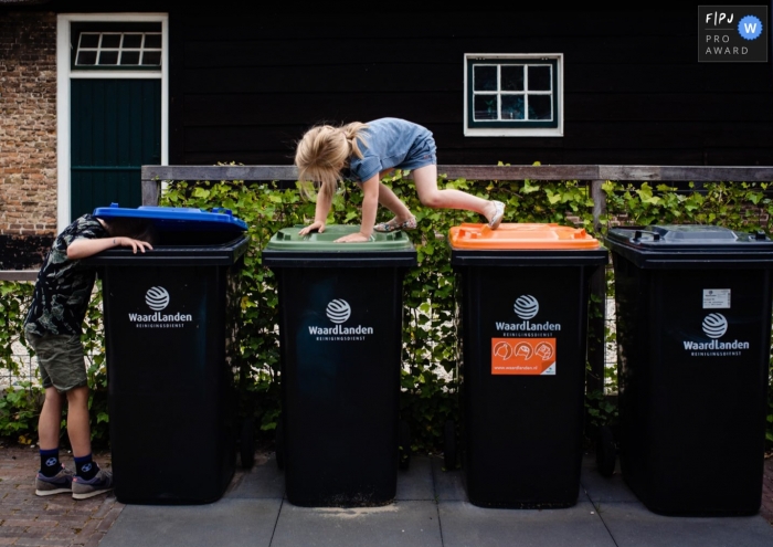Moment driven Netherlands family photojournalism image of kids hoping over trash cans Moment driven Netherlands family photojournalism image of kids hoping over trash cans