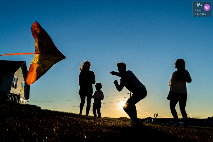 Image de photojournalisme familial du New Hampshire entraînée par le moment d'une famille faisant voler un cerf-volant du Roi Lion au coucher du soleil dans le Maine