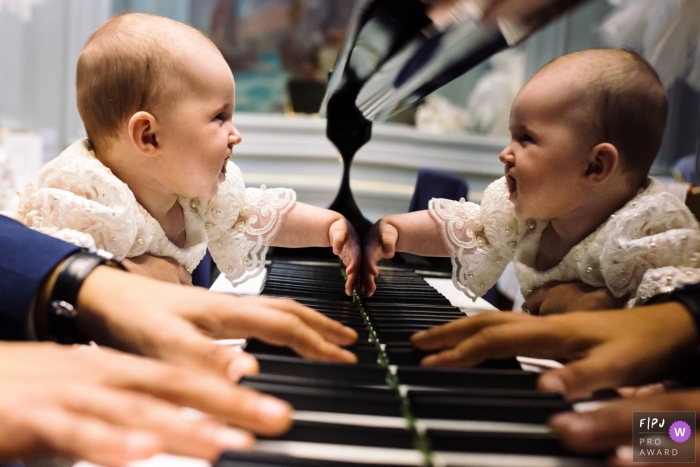 Image de photojournalisme familial à Paris, animée par un moment, d'un bébé regardant son reflet sur un piano