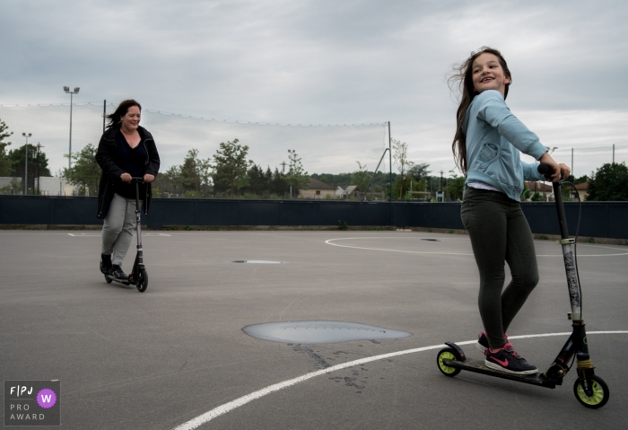 Moment driven Nimes family photojournalism image of a mom and daughter on scooter Moment driven Nimes family photojournalism image of a mom and daughter on scooter