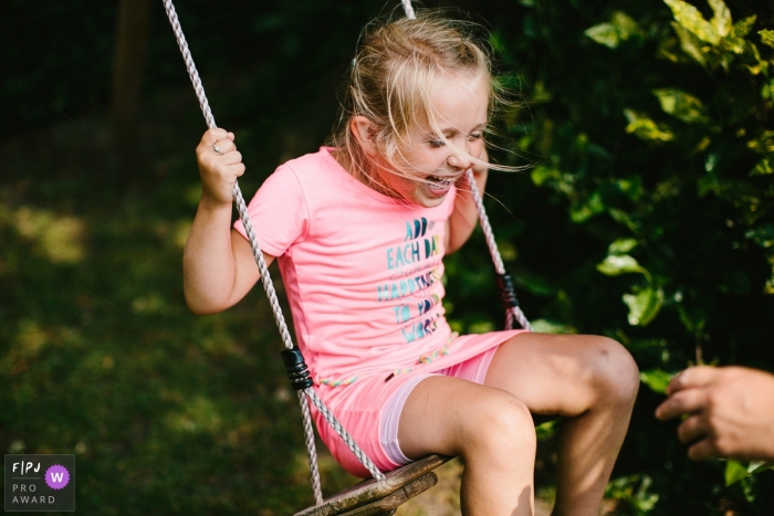 Moment driven Drenthe family photojournalism image of a girl swinging with laughter Moment driven Drenthe family photojournalism image of a girl swinging with laughter
