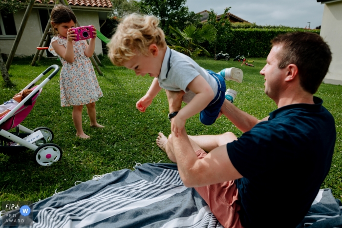 Moment-driven Occitanie family photography of dad and his children playing outside in the yard Moment-driven Occitanie family photography of dad and his children playing outside in the yard