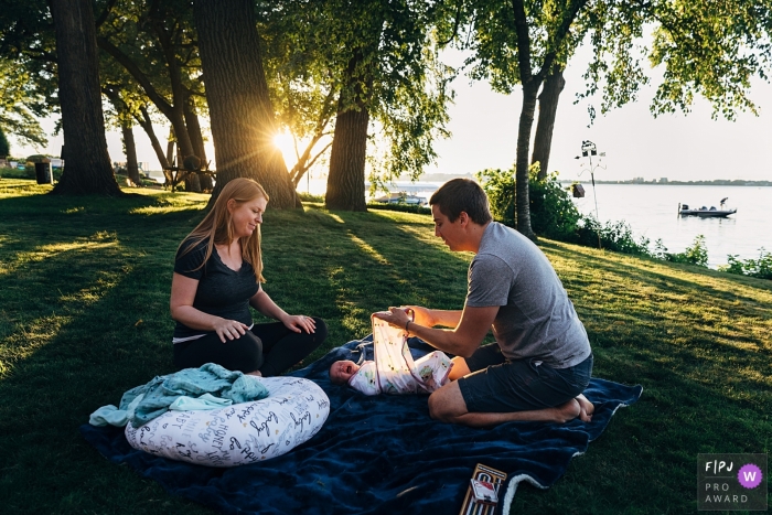 Momentgedreven fotojournalistiek van de familie uit Wisconsin, waarop ouders hun pasgeboren baby kalmeren en inbakeren in hun achtertuin aan het meer