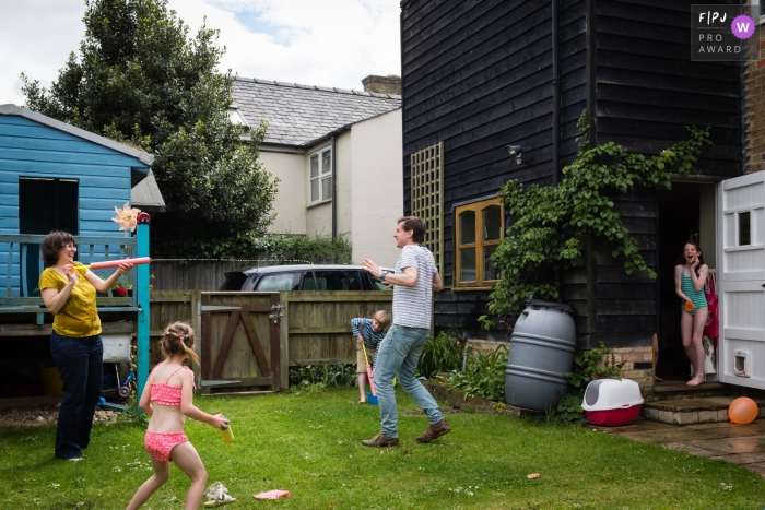 Moment-driven Cambridgeshire family photography showing Mum shoots Dad with a water pistol in the garden while their children look on and laugh