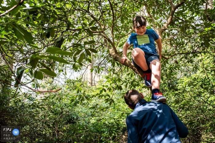 Moment-driven East Flanders family photography showing dad helping child down from a tree