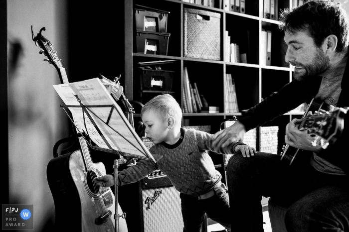 Moment driven Belgium family photojournalism image in BW of dad playing music on guitars with young son