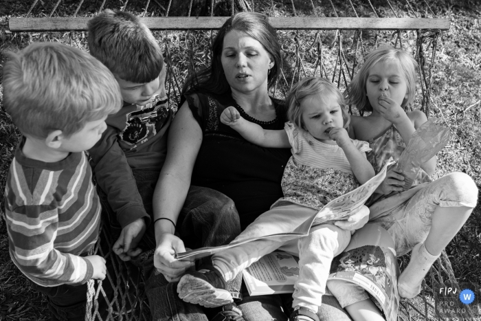 Moment-driven Connecticut family photography showing A mother reads a story to her children in a hammock Moment-driven Connecticut family photography showing A mother reads a story to her children in a hammock