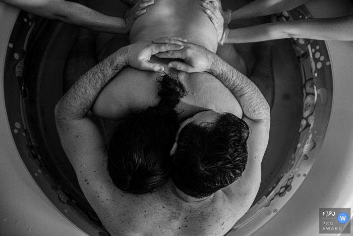 Séance photo d'accouchement à domicile à Sao Paulo couvrant une femme accueillie par son partenaire et recevant l'aide d'une sage-femme et d'une doula avec une pression sur la hanche pour soulager la contraction