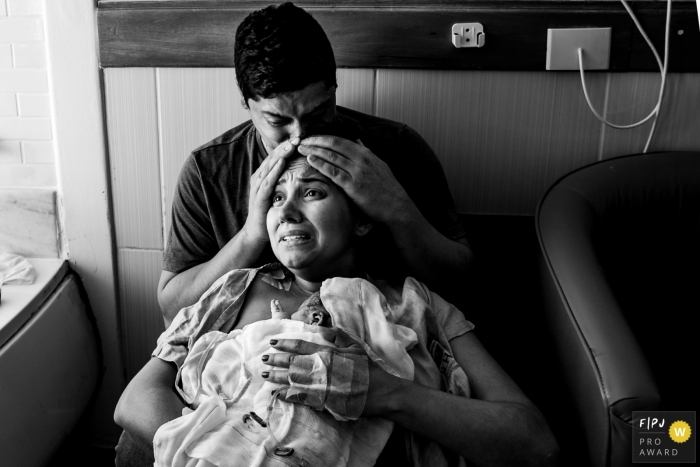 Maternidade Ilha birth image of a very emotional mother as she holds her new baby and is being kissed on his head by her husband Maternidade Ilha birth image of a very emotional mother as she holds her new baby and is being kissed on his head by her husband