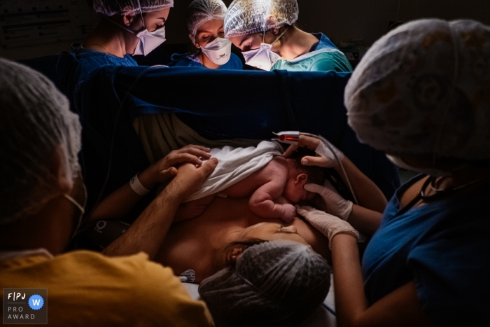 Sao Paulo birthing image of the mother receiving the newborn as medical staff in the background work on the mother Sao Paulo birthing image of the mother receiving the newborn as medical staff in the background work on the mother