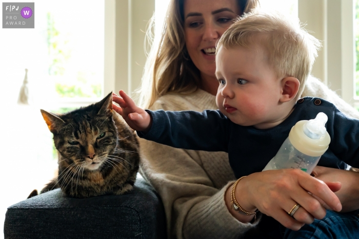 Zuid Holland family photo of a young boy taking a break from his bottle to reach out to his cat Zuid Holland family photo of a young boy taking a break from his bottle to reach out to his cat