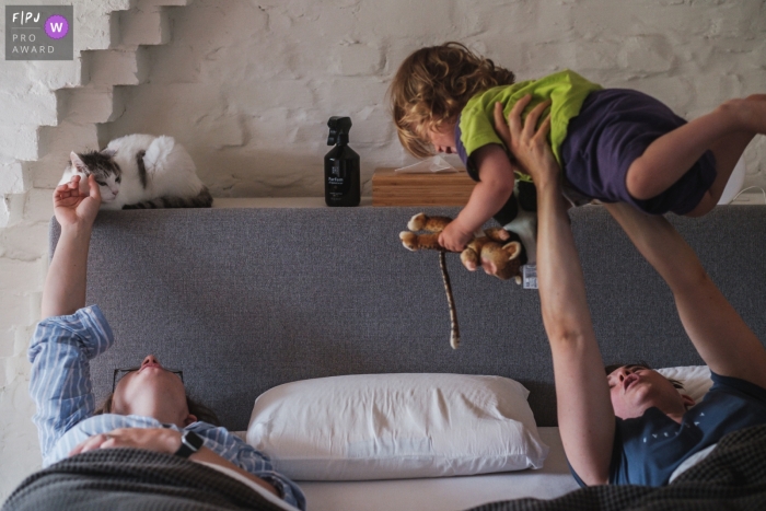 Antwerpen family photo of a One mom pets the cat, while the other plays with the daughter, in bed Antwerpen family photo of a One mom pets the cat, while the other plays with the daughter, in bed