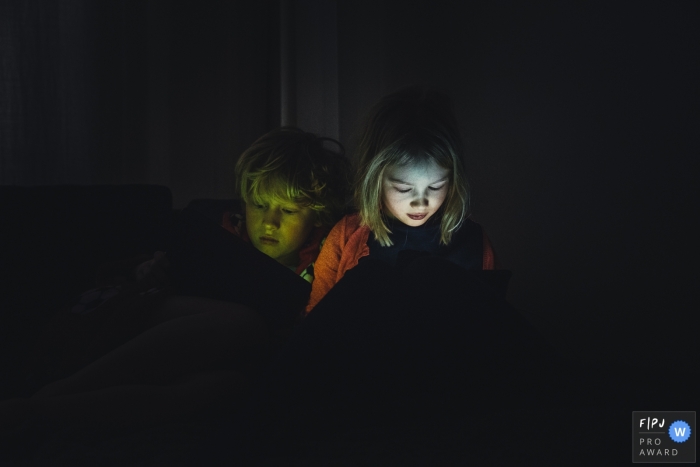 Amsterdam family photo of a boy and girl looking at an iPad with their faces lit up in the dark