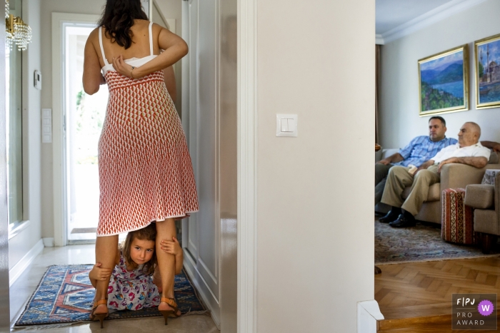 Istanbul family photography of a young girl hiding under her mom's legs, and the men are seen in the livingroom watching television