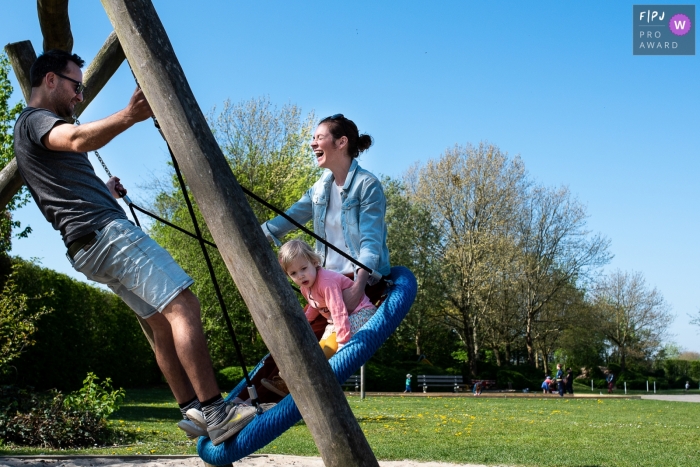 East Flanders day in the life photo of a father, mother and young child swinging together East Flanders day in the life photo of a father, mother and young child swinging together