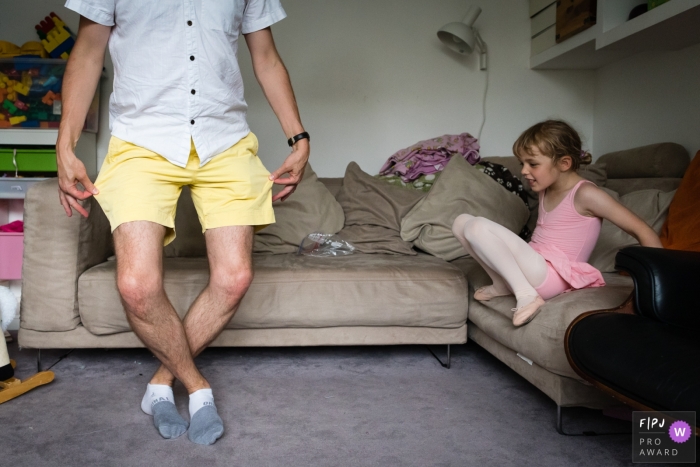 Image de la famille Cambridgeshire d'une fille prenant une pause dans la pratique du ballet pour regarder son père tenter un mouvement de ballet