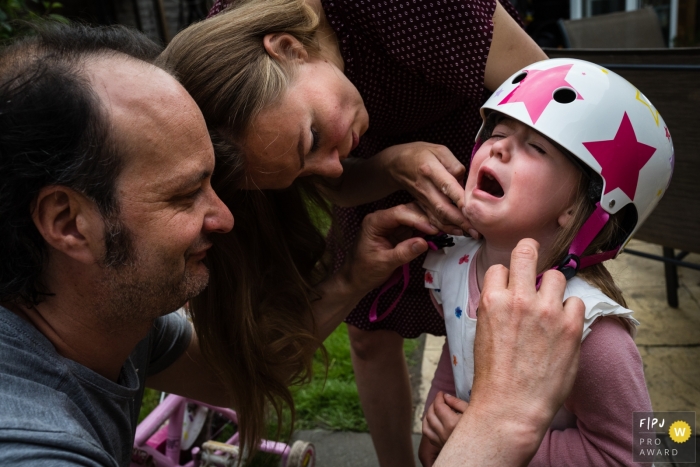 Familienfoto aus Cambridgeshire, das Eltern zeigt, wie sie ihre Tochter trösten, die sich beim Aufsetzen ihres Fahrradhelms den Hals verletzt hat