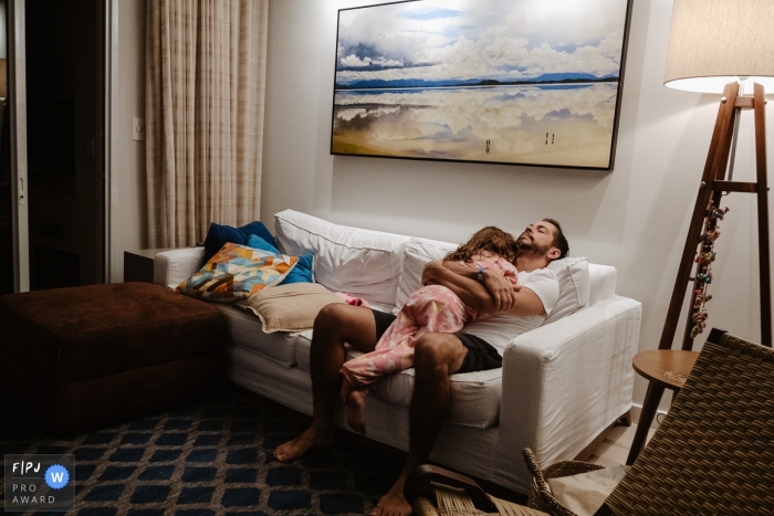 Florianopolis at-home photo of a tired father with his daughter on the couch in the house Florianopolis at-home photo of a tired father with his daughter on the couch in the house