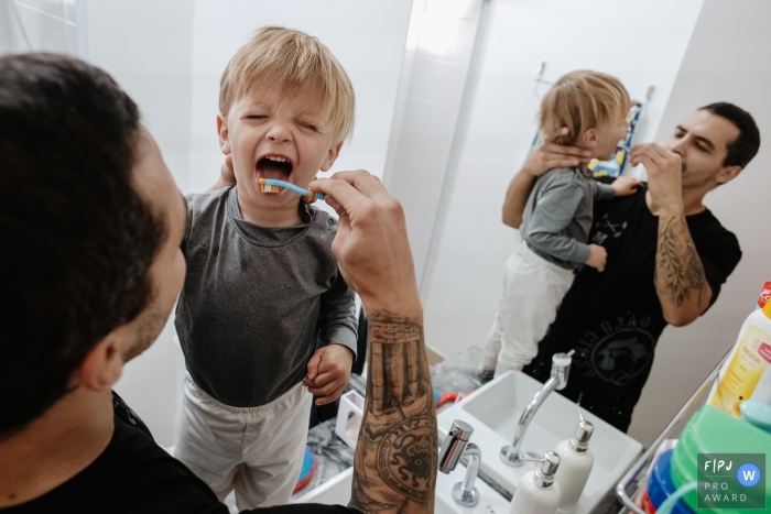 Santa Catarina father brushing his son's teeth in front of the bathroom mirror during an at-home photo session Santa Catarina father brushing his son's teeth in front of the bathroom mirror during an at-home photo session