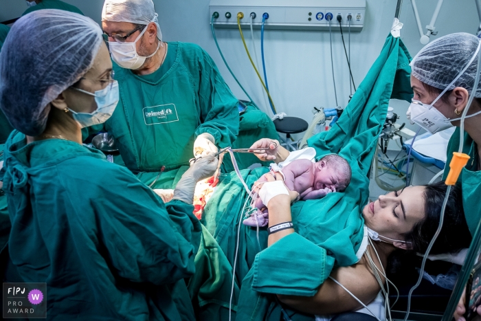 A Campos dos Goytacazes birth photographer at Hospital Unimed Campos captured this image of mother cutting the cord in the surgery room A Campos dos Goytacazes birth photographer at Hospital Unimed Campos captured this image of mother cutting the cord in the surgery room