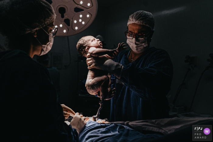 Florianopolis dokumentarische Geburtsfotografie in der Maternidade Santa Helena eines kleinen Jungen, der vom Arzt unter den OP-Leuchten gehalten wird