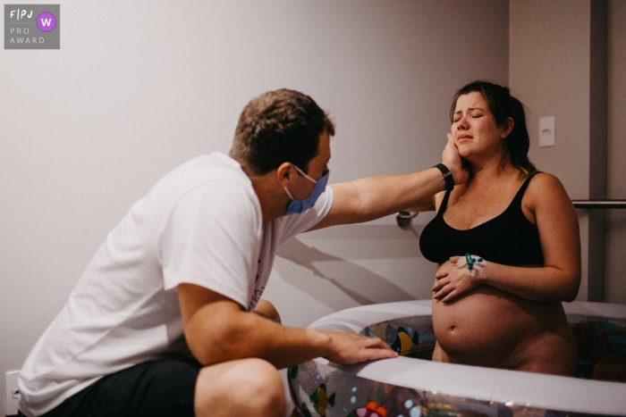 Ein Florianopolis-Geburtsfotograf in Maternidade Ilha hat diese Mutter in einer Wasserbadewanne dokumentiert, während ihr Vater ihr Gesicht hielt