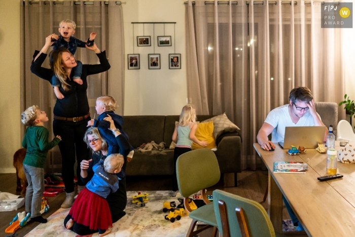 Ein dokumentarischer Familienfotograf aus Flevoland hat dieses Familienchaos mit Papa auf einem Computer und Kindern, die in seiner Nähe spielen, festgehalten