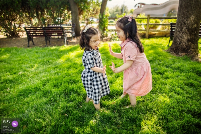 Photo by: <a href="https://www.fpja.com/documentary-family-photography-contests/chris-shum/san-francisco/2115195">Chris Shum - United States</a> San Francisco documentary family photography of girls on the grass playing pat a cake sis