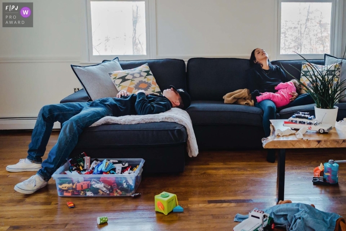 Dokumentarische Familienfotografie aus New Hampshire, die zeigt, wie Mama, Papa und Baby auf einer Couch mit Spielzeug rundherum ein kurzes Nickerchen machen