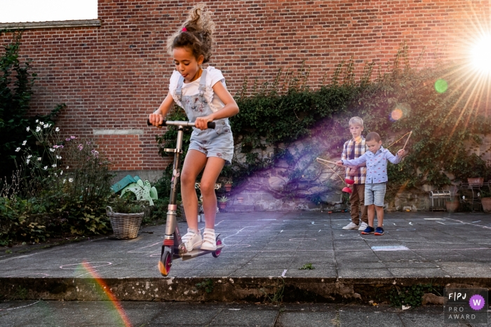 Photo by: <a href="https://www.fpja.com/documentary-family-photography-contests/emilie-marchandise/wallonie/2115314">Emilie Marchandise - Belgium</a> A Wallonie, Belgium documentary family photographer chronicled siblings playing with a Razor scooter in the sunlight