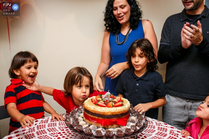 Belo Horizonte documentary family photography showing the boy pushes his little brother so he cant blow out his birthday candle in a hilarious scene