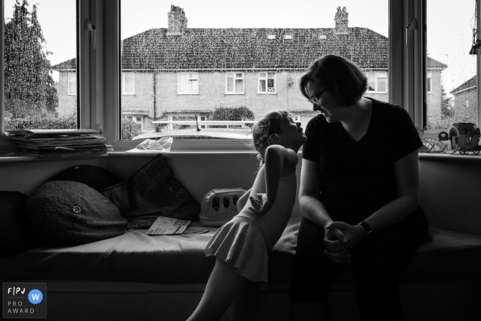 Photo by: <a href="https://www.fpja.com/documentary-family-photography-contests/alice-chapman/cambridgeshire/2116078">Alice Chapman - United Kingdom</a> Cambridgeshire documentary family photography chronicling A mother and daughter smiling at each other in their living room while it rains outside